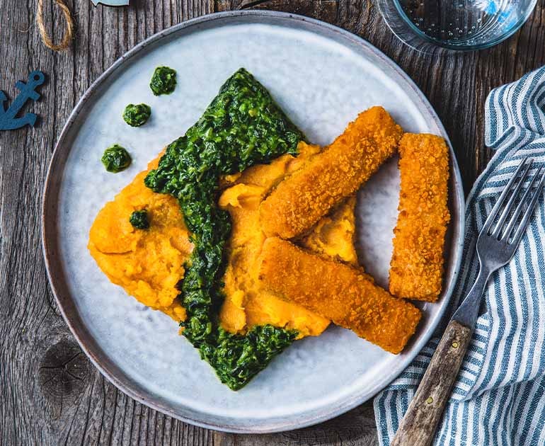 Fischstäbchen, Süßkartoffelbrei und Spinat als Fisch angerichtet auf einem Teller